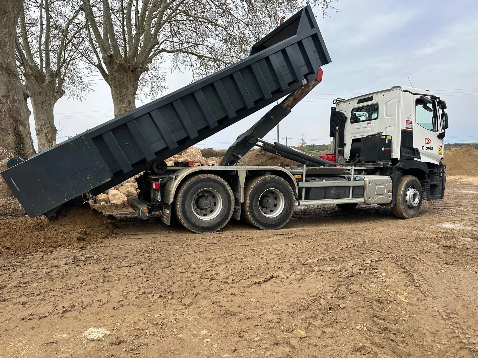Camion-benne au caisson relevé sur un terrain en terre avec des tas de matériaux