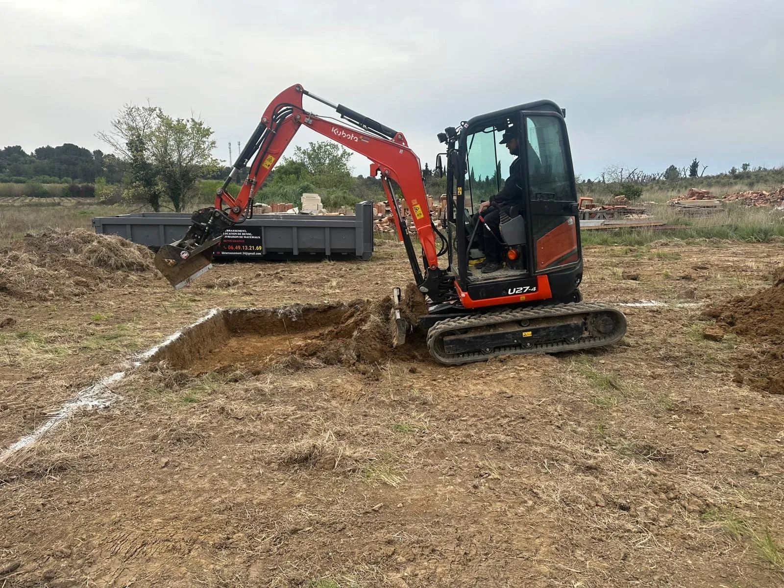 Mini-pelle Kubota avec conducteur creusant une tranchée sur un terrain