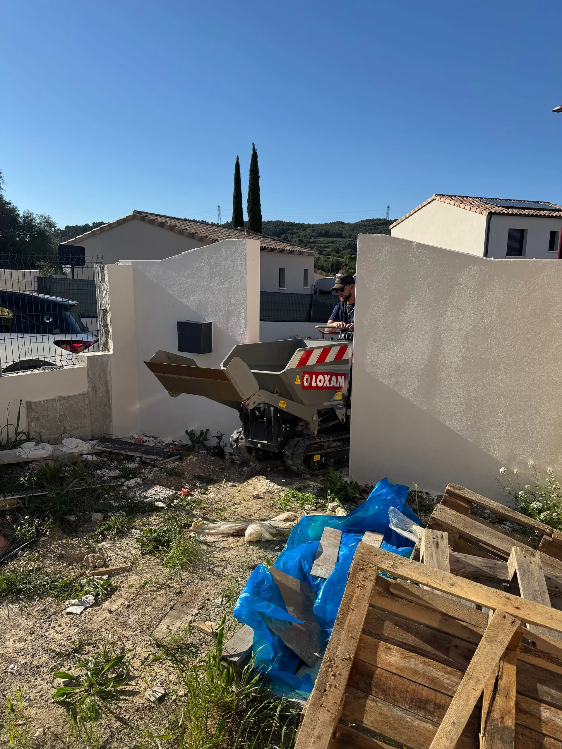 Opérateur conduisant un mini-dumper à chenilles chargé de gravats sur un chantier résidentiel.