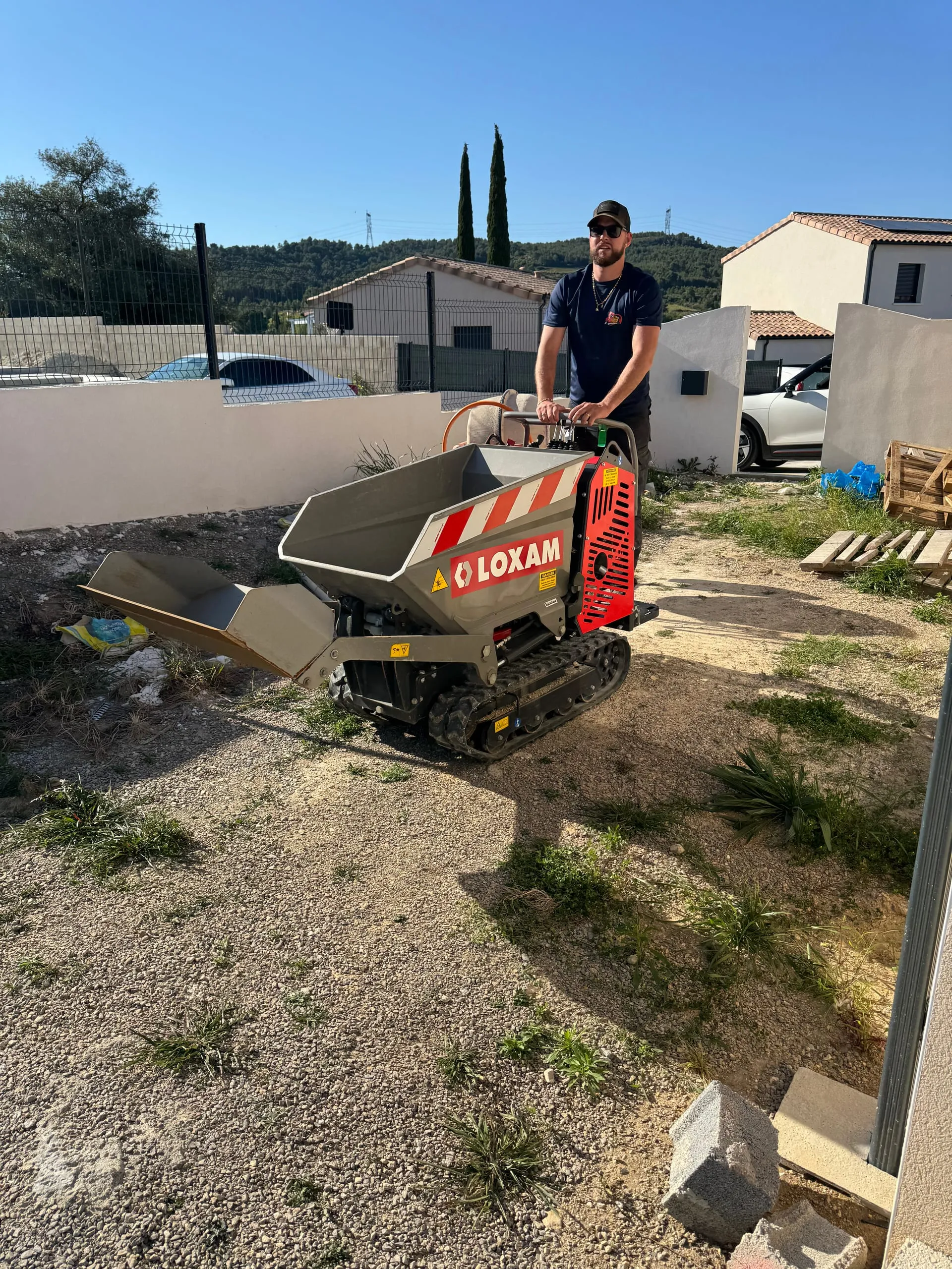 Opérateur de terrassement conduisant un mini-dumper sur chenilles sur un terrain résidentiel.