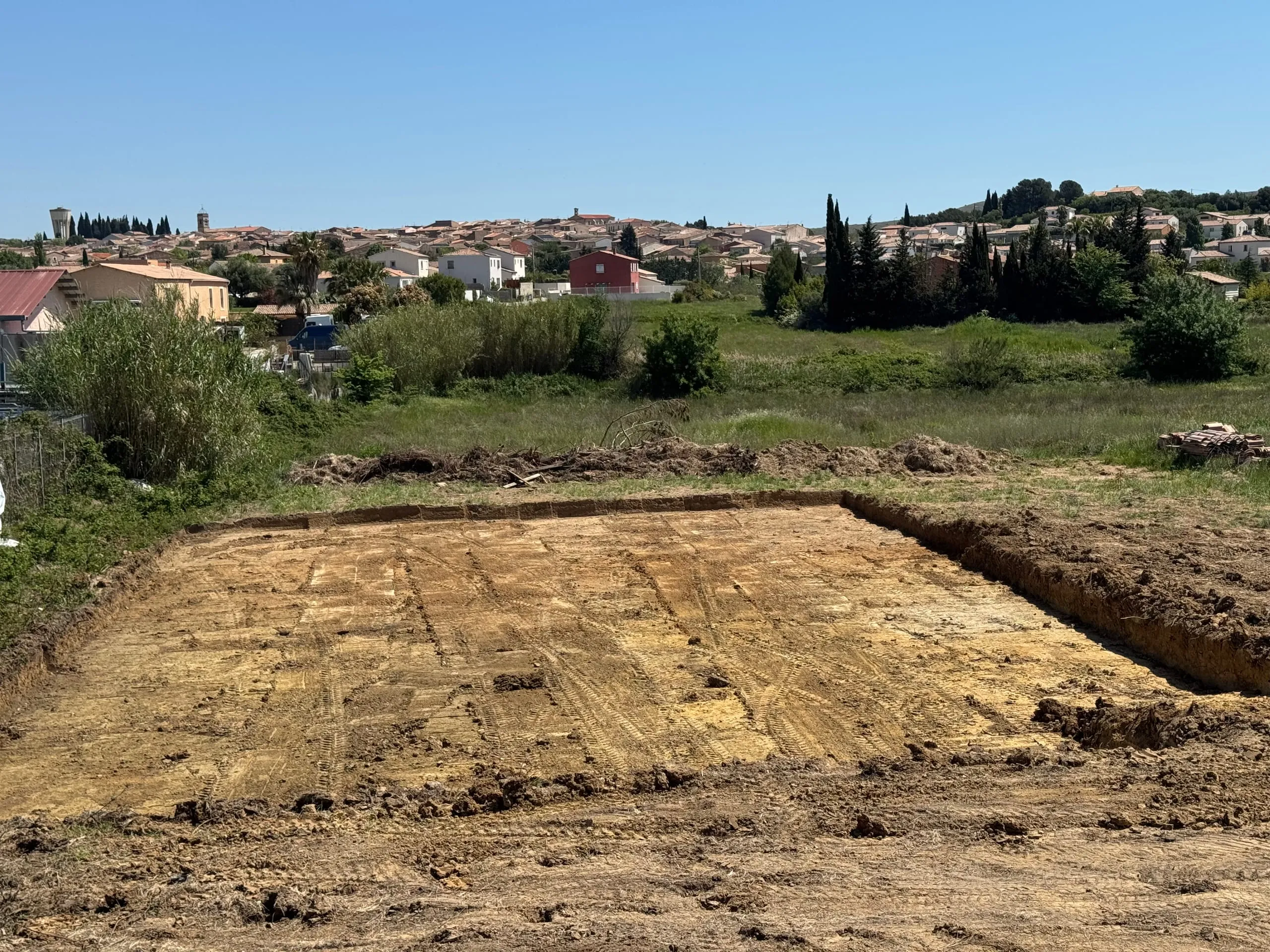 Terrassement d'une plateforme de terrain décapé et nivelé, avec un village en arrière-plan.