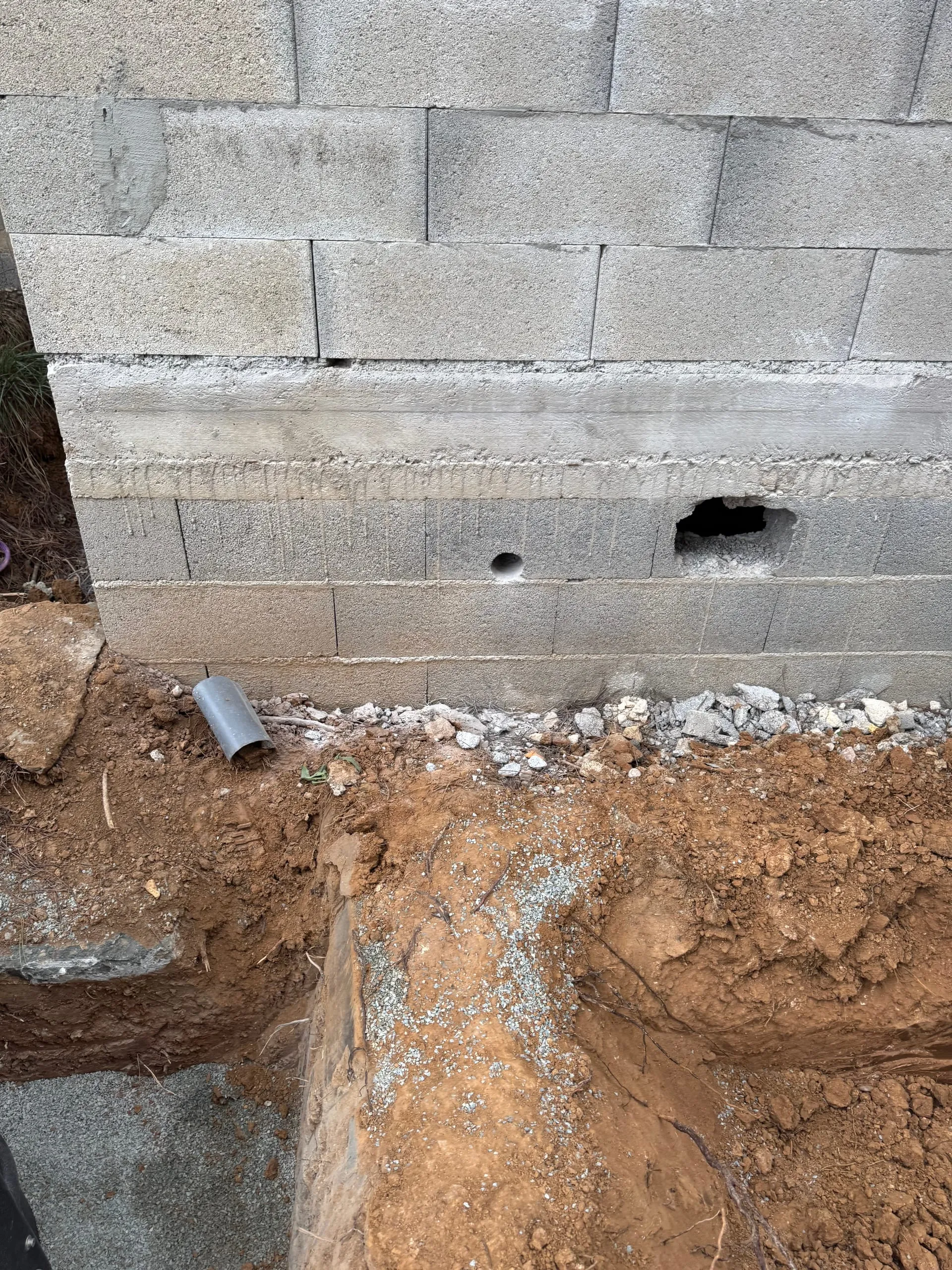 Tranchée de terrassement au pied d’un mur en blocs béton avec un tuyau apparent