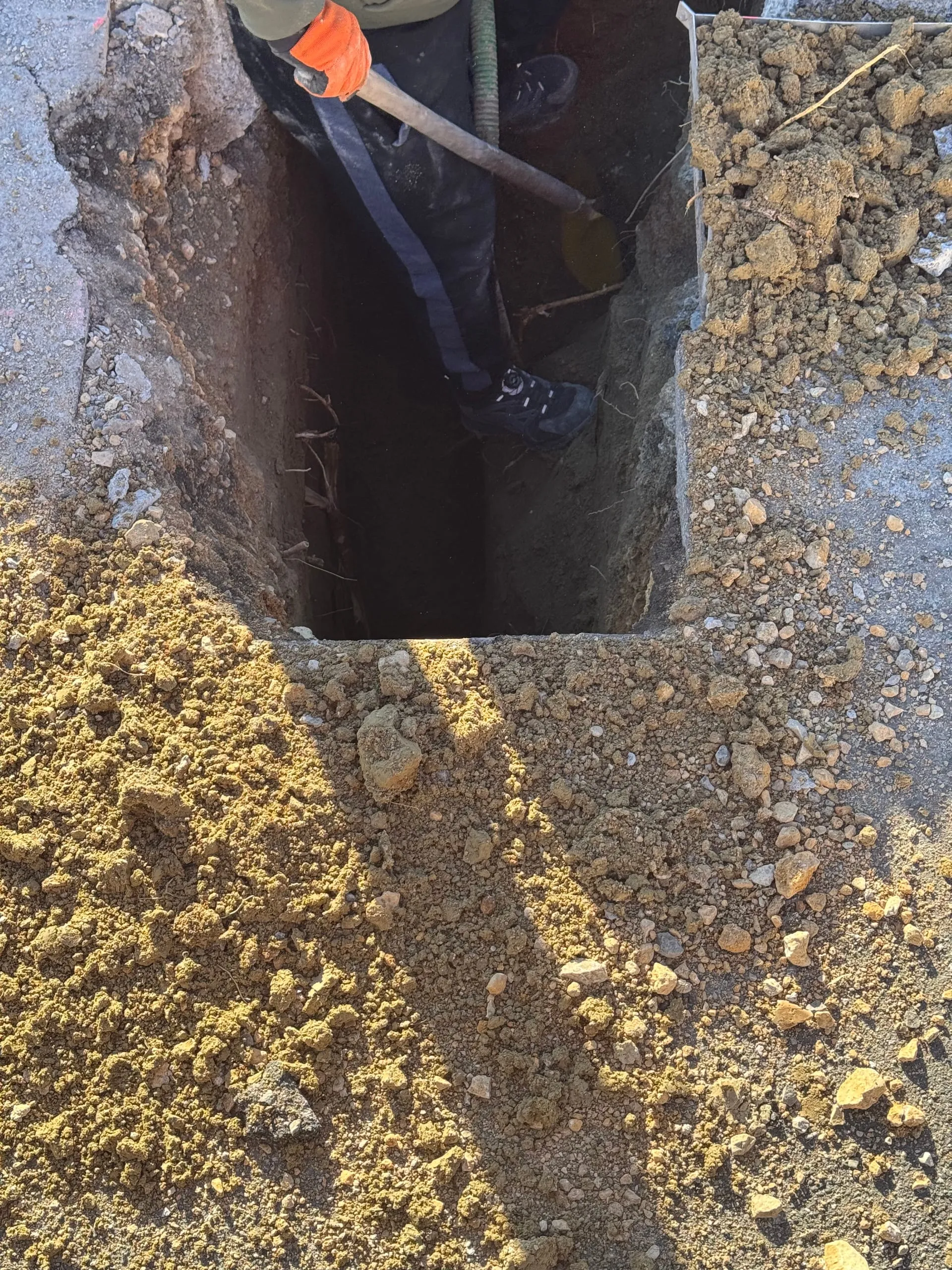 Ouvrier équipé creusant une tranchée étroite dans un sol rocailleux