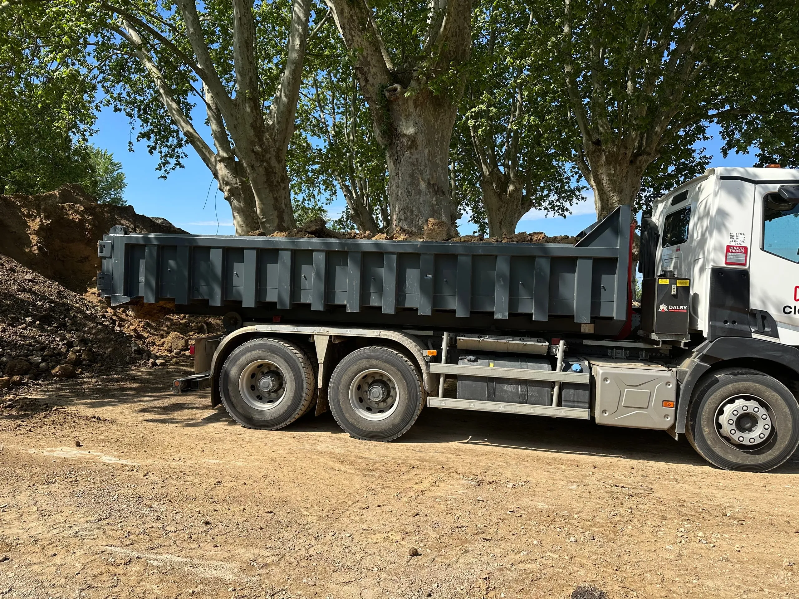 Camion-benne chargé de terre, stationné sur un terrain en travaux sous de grands arbres