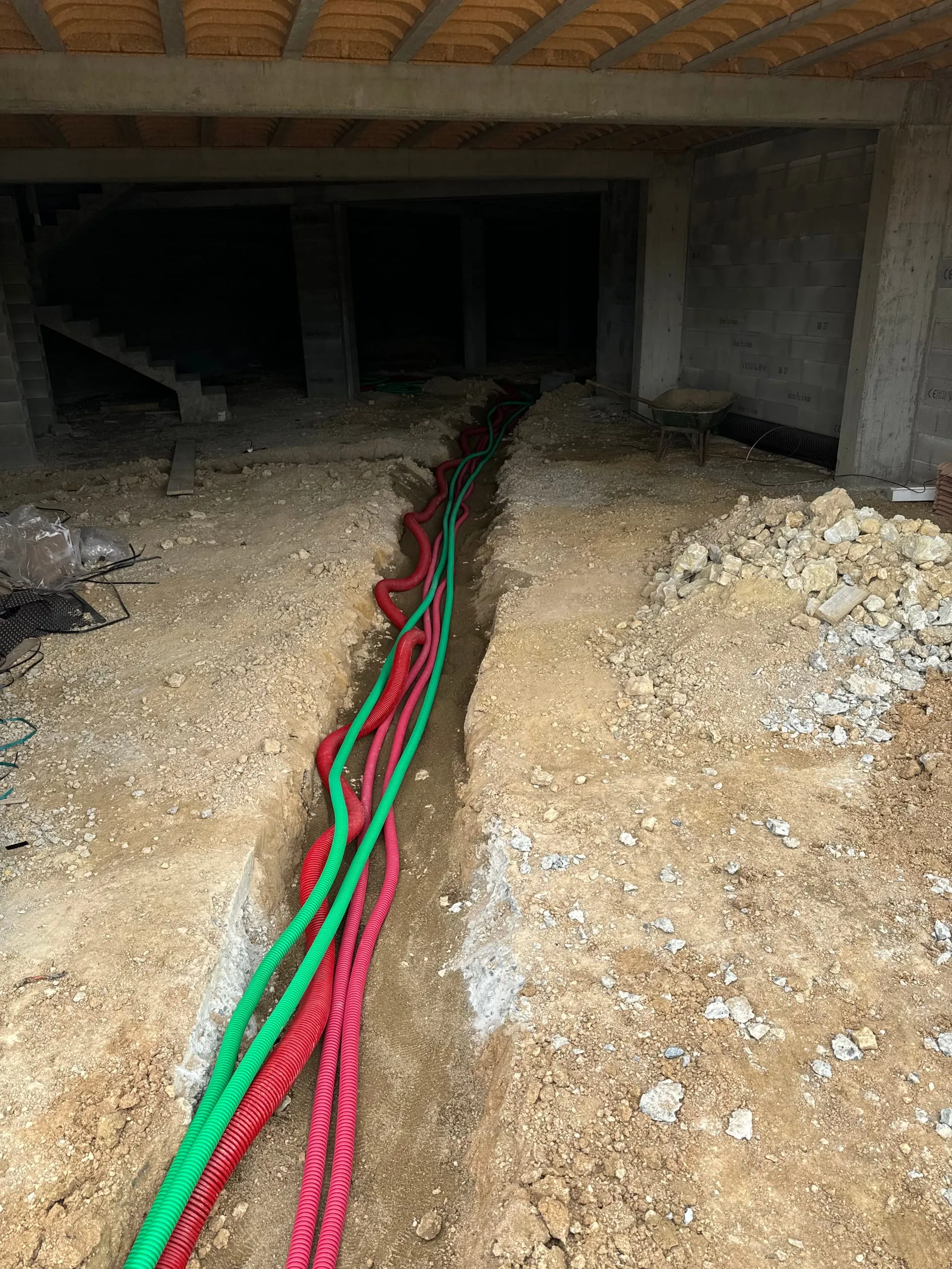 Tranchée et passage de gaines rouges et vertes dans un bâtiment en construction