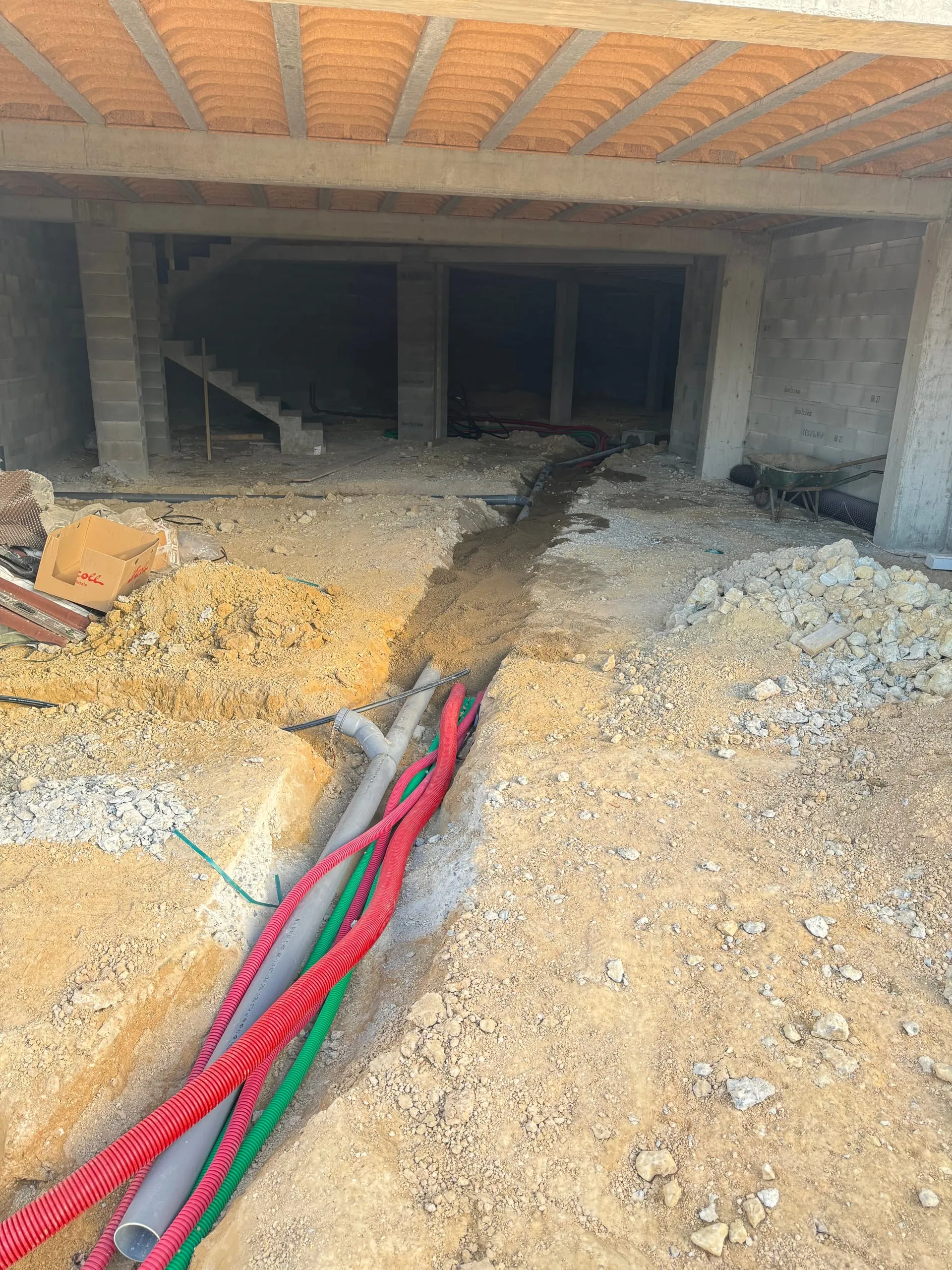 Passage de gaines électriques, fibre et eau dans une tranchée intérieure en cours de terrassement