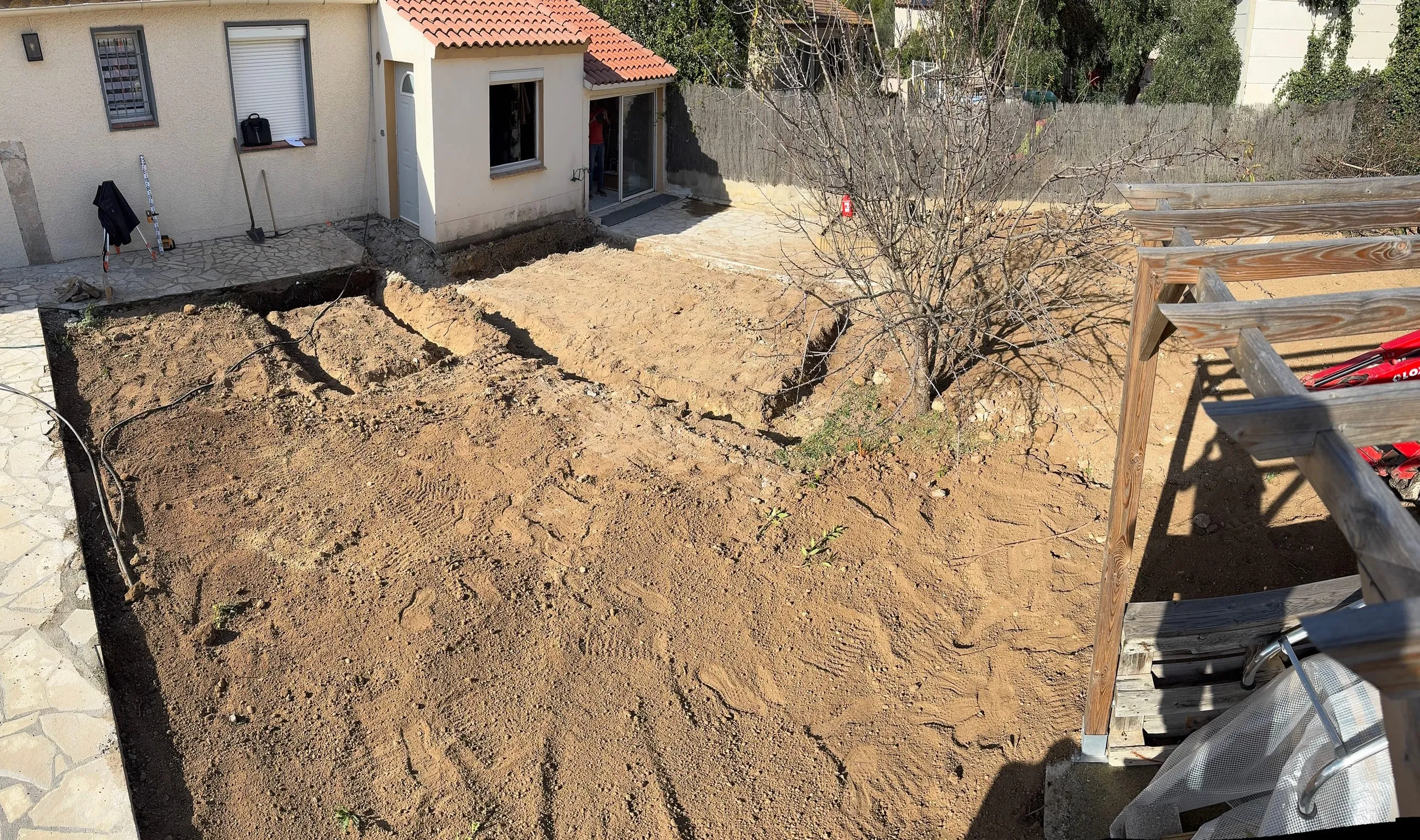 Jardin décapé au pied d’une maison avec des tranchées ouvertes et un engin de chantier
