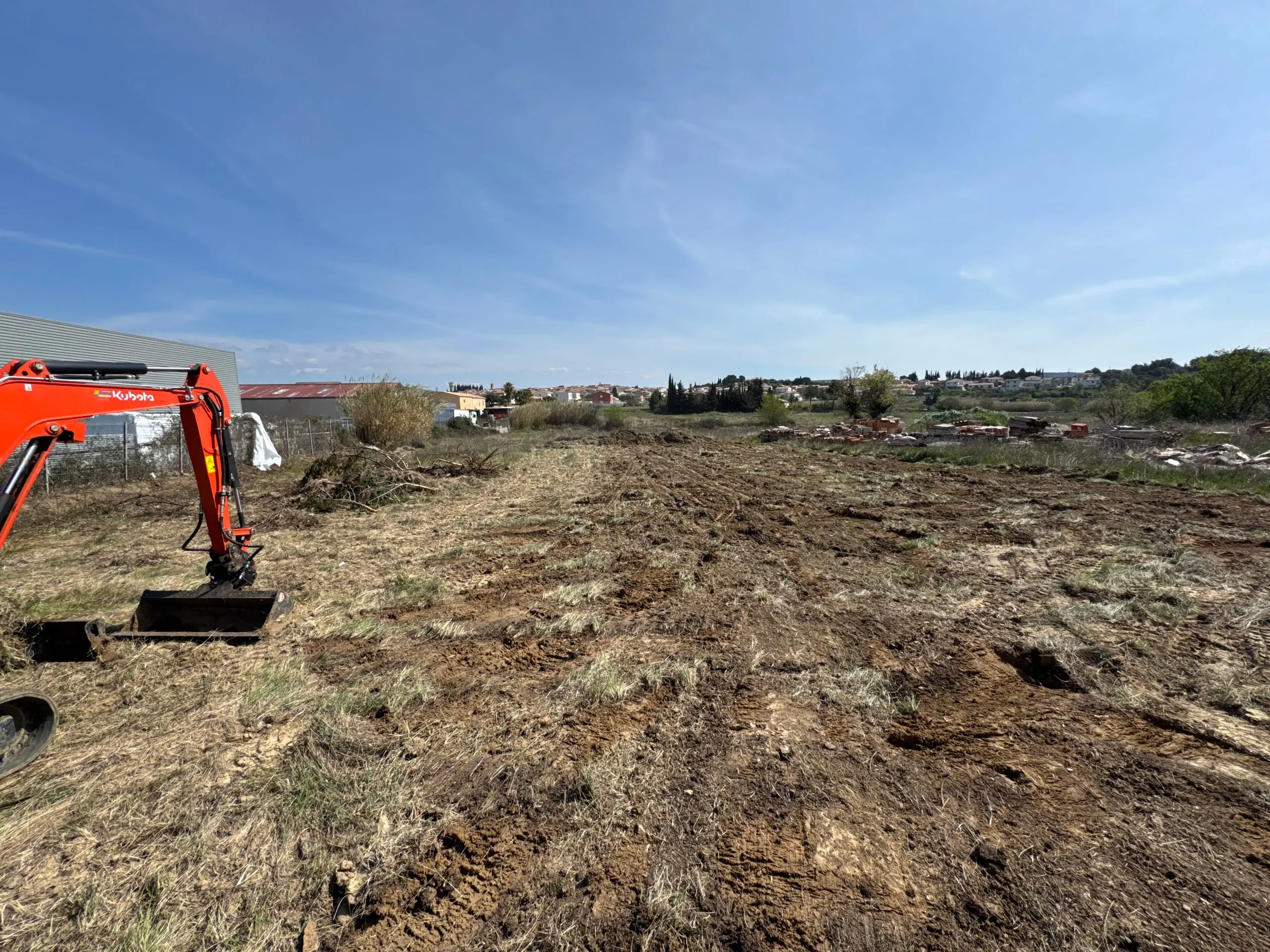 Pelle mécanique orange sur un terrain en cours de préparation pour des travaux de terrassement.