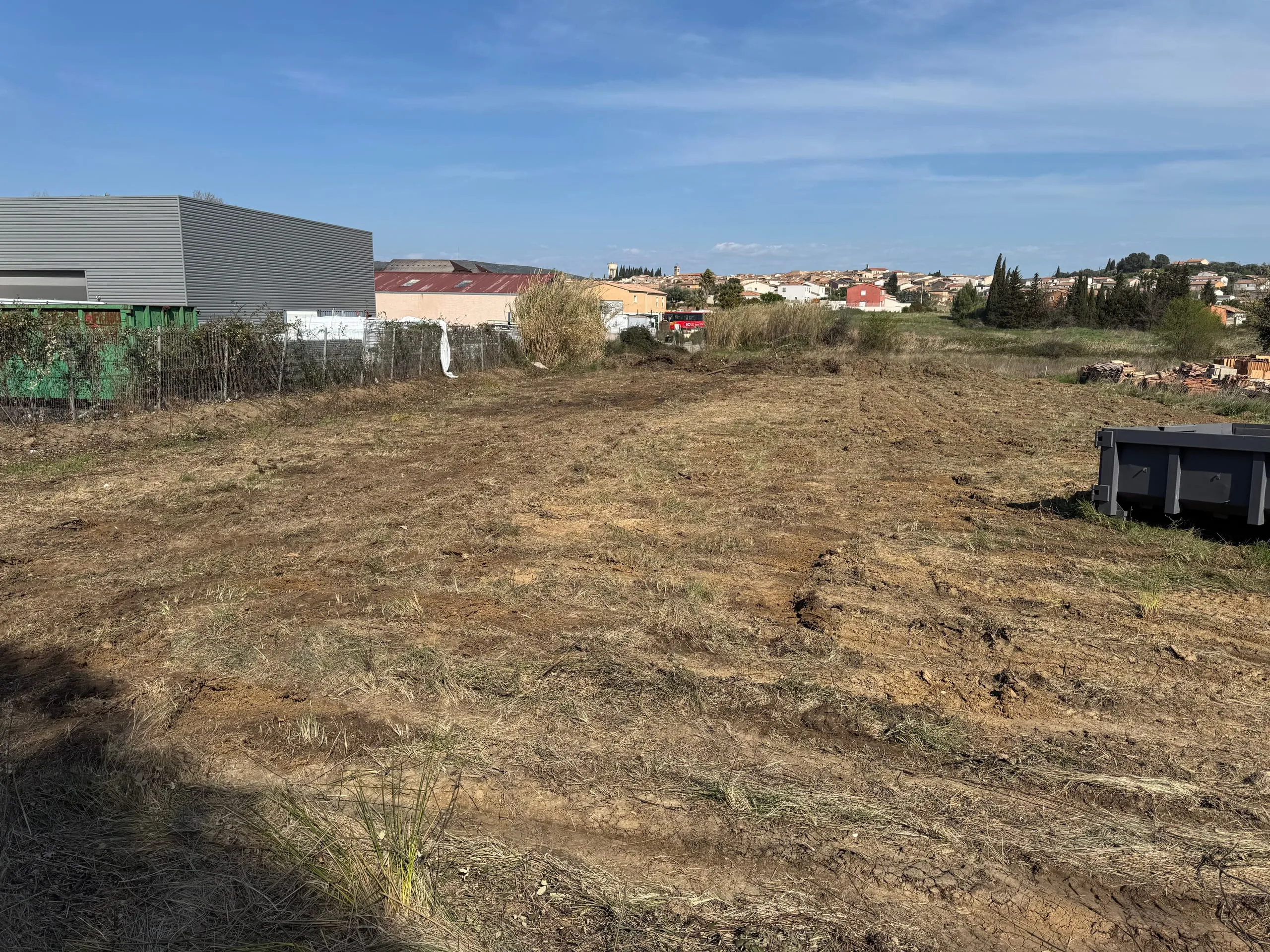 Terrain dégagé et travaillé, avec une benne et une zone bâtie en arrière-plan