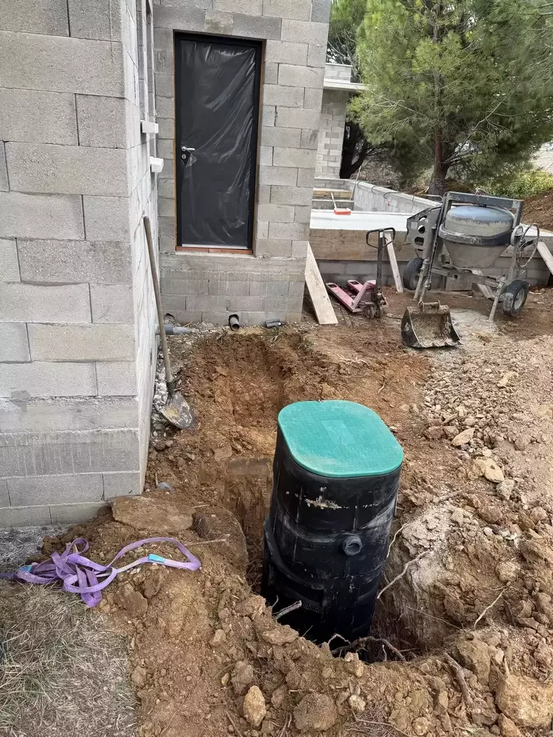 Regard technique installé dans une excavation près d’une construction en parpaings