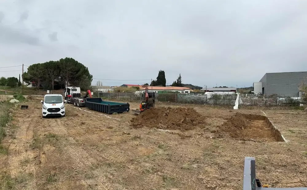 Terrain décaissé avec un important volume de terre, une mini-pelle, une benne et des véhicules de chantier
