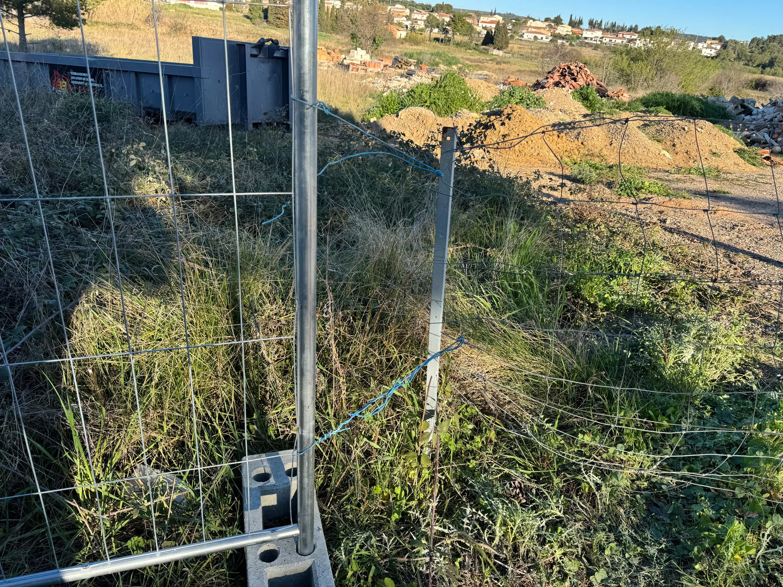 Benne de chantier sombre au bord d’un terrain, près de tas de terre et de gravats