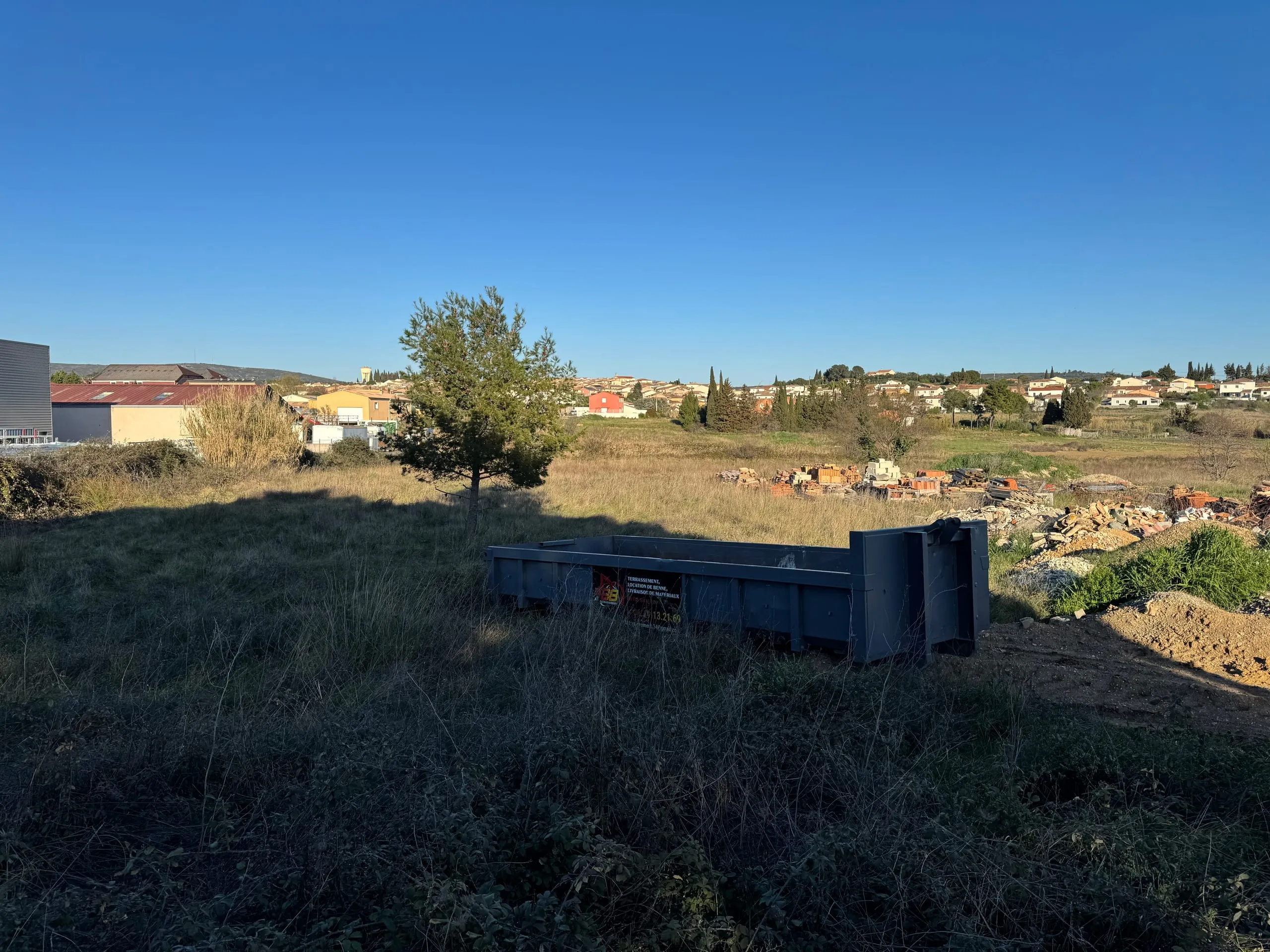 Benne de chantier installée sur un terrain herbeux près de gravats