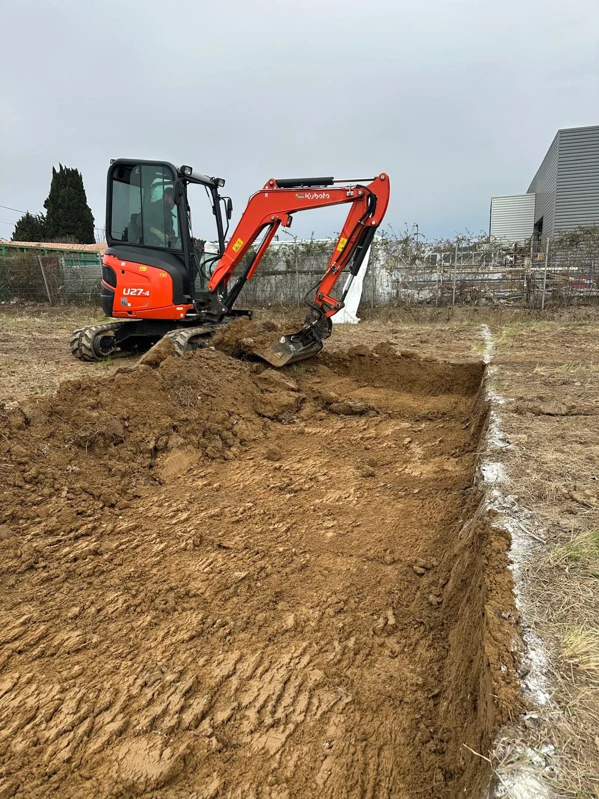 Décaissement d'un terrain à la mini-pelle devant un bâtiment industriel.