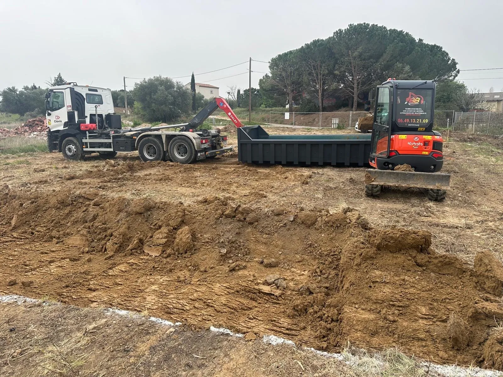 Camion porteur, benne ouverte et mini-pelle Kubota sur un terrain en cours de terrassement