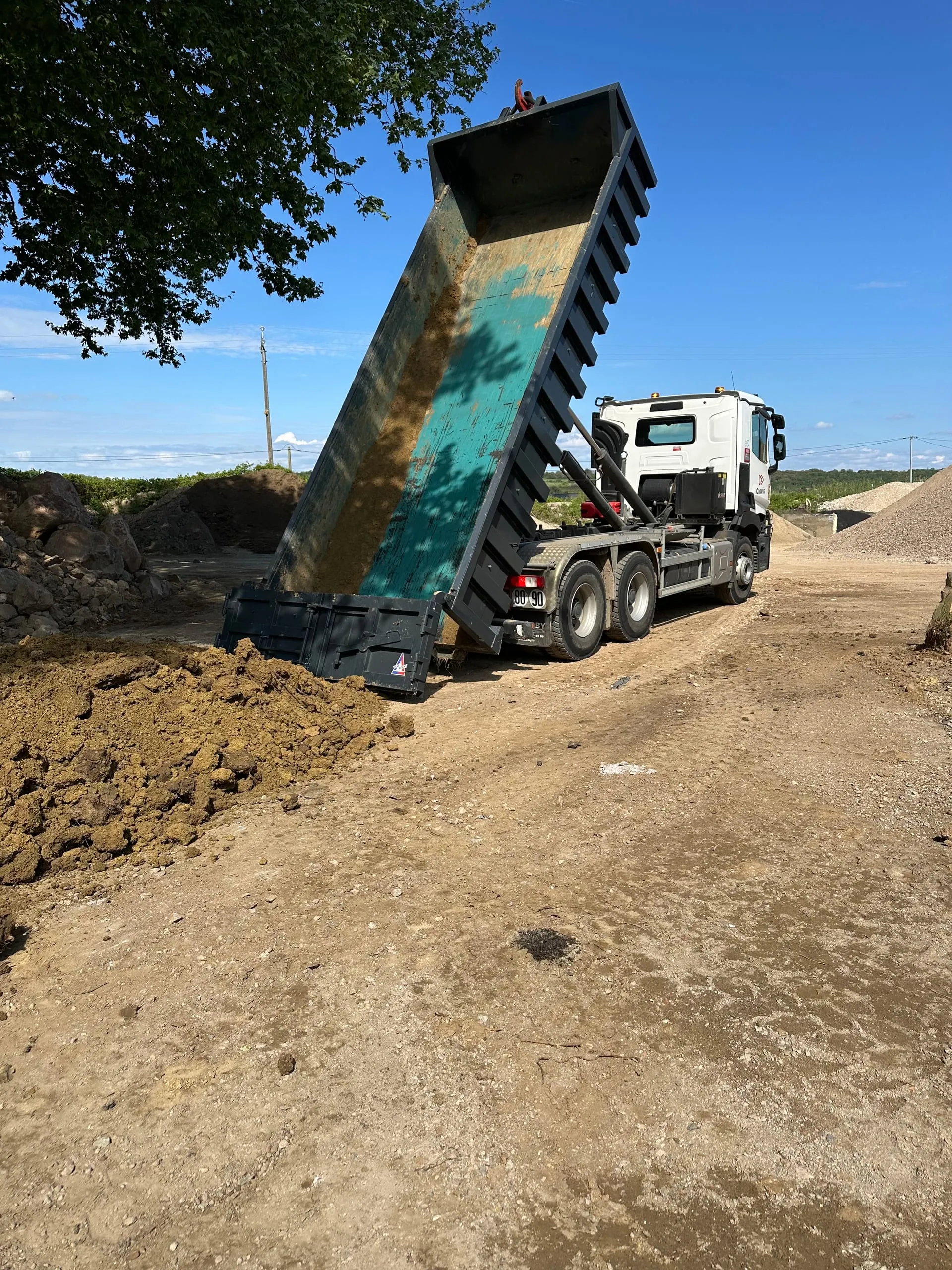 Camion-benne au caisson relevé devant des tas de granulats