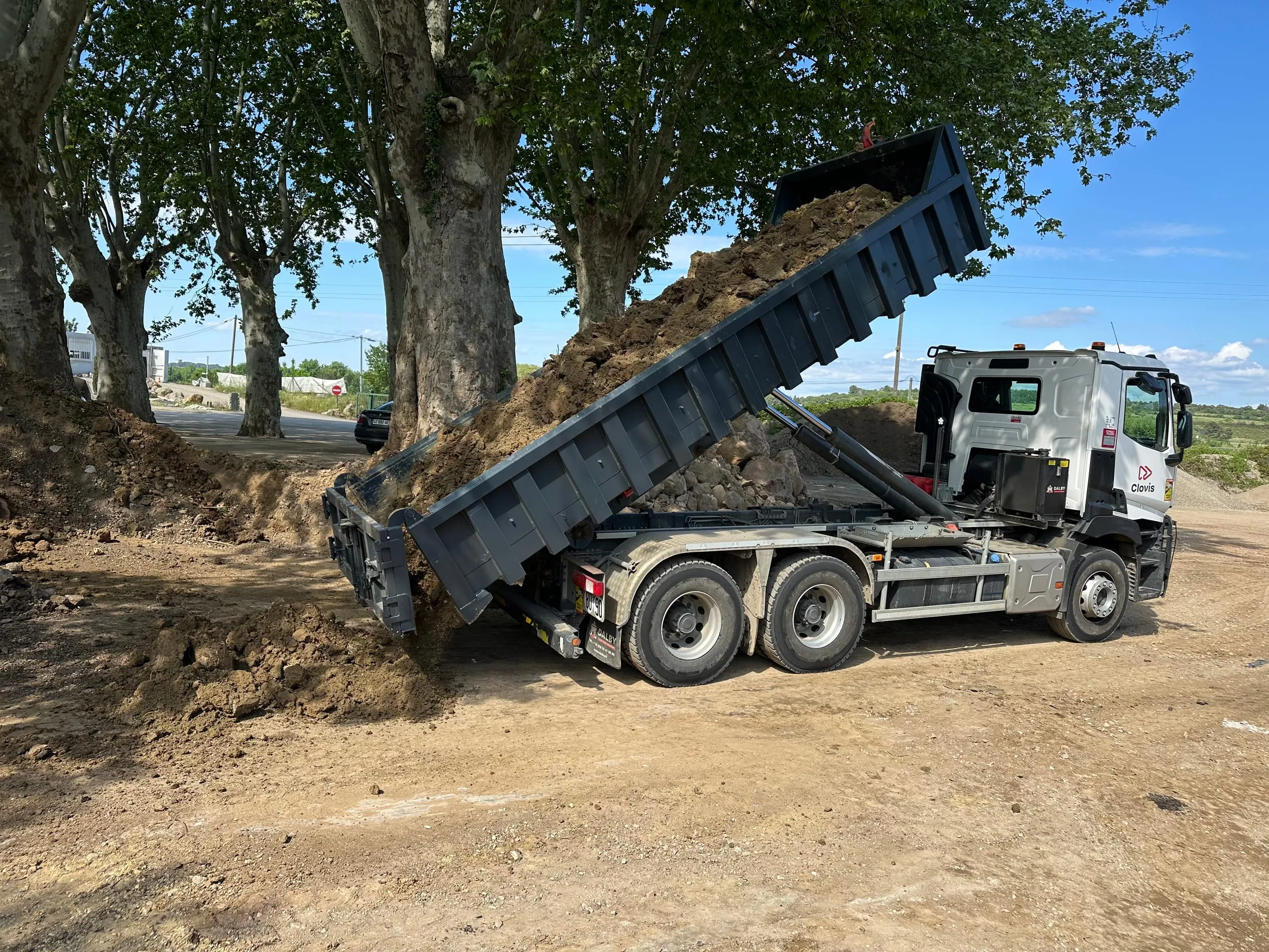 Camion-benne déversant de la terre sur un terrain arboré