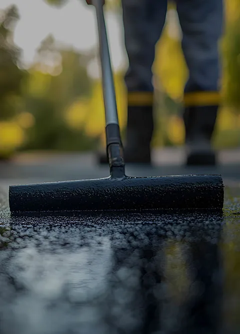 Ouvrier utilisant un rouleau applicateur pour étaler de l’enrobé noir sur une surface extérieure