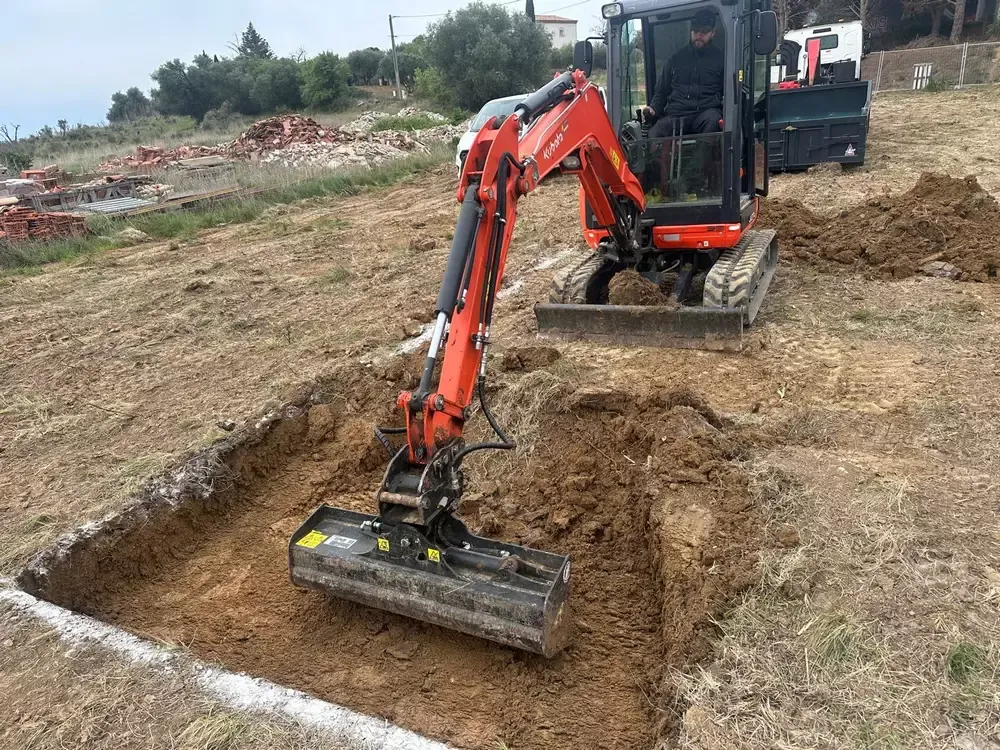 Mini-pelle orange creusant un terrain délimité pour un terrassement